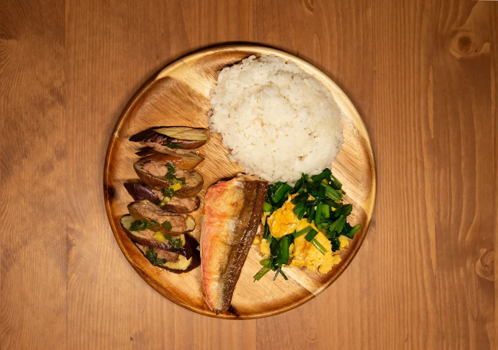Grilled fish with rice, greens and other vegetables on a round wooden plate