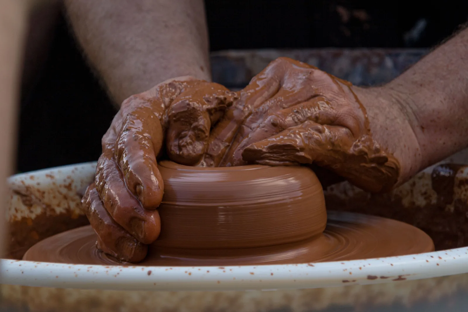 Clay-covered hands shaping a pot on a potter's wheel