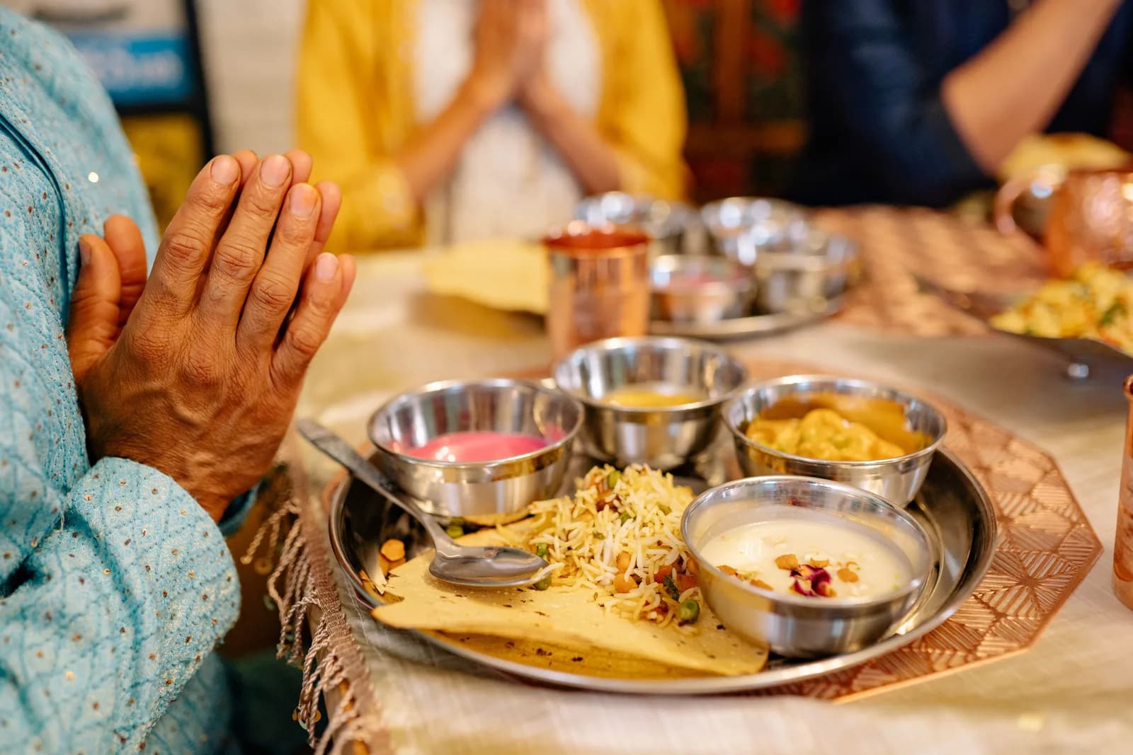 Hands pressed together in thanks before a steel thali of small dishes