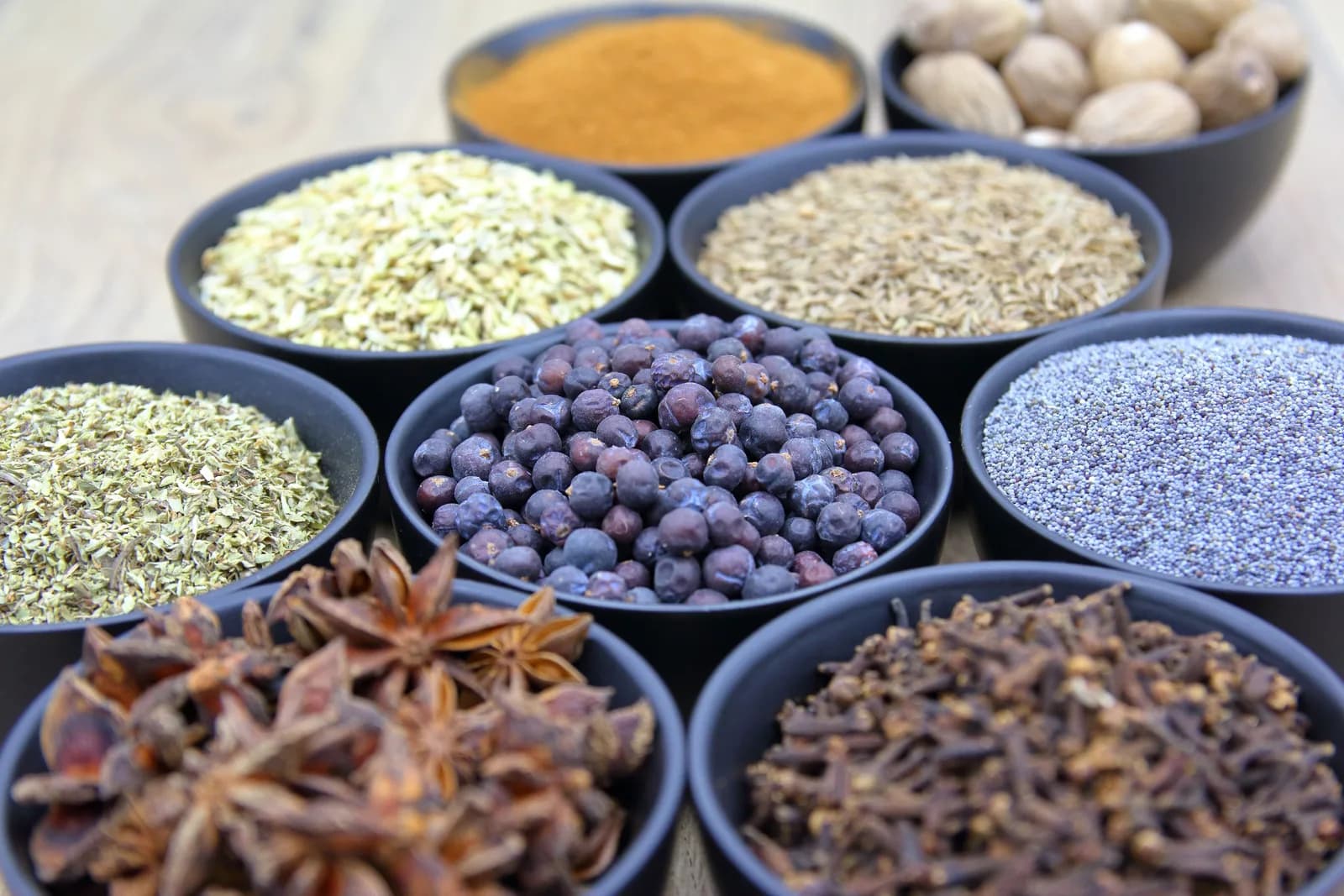 Black bowls of whole spices, including star anise, cloves and several kinds of seeds