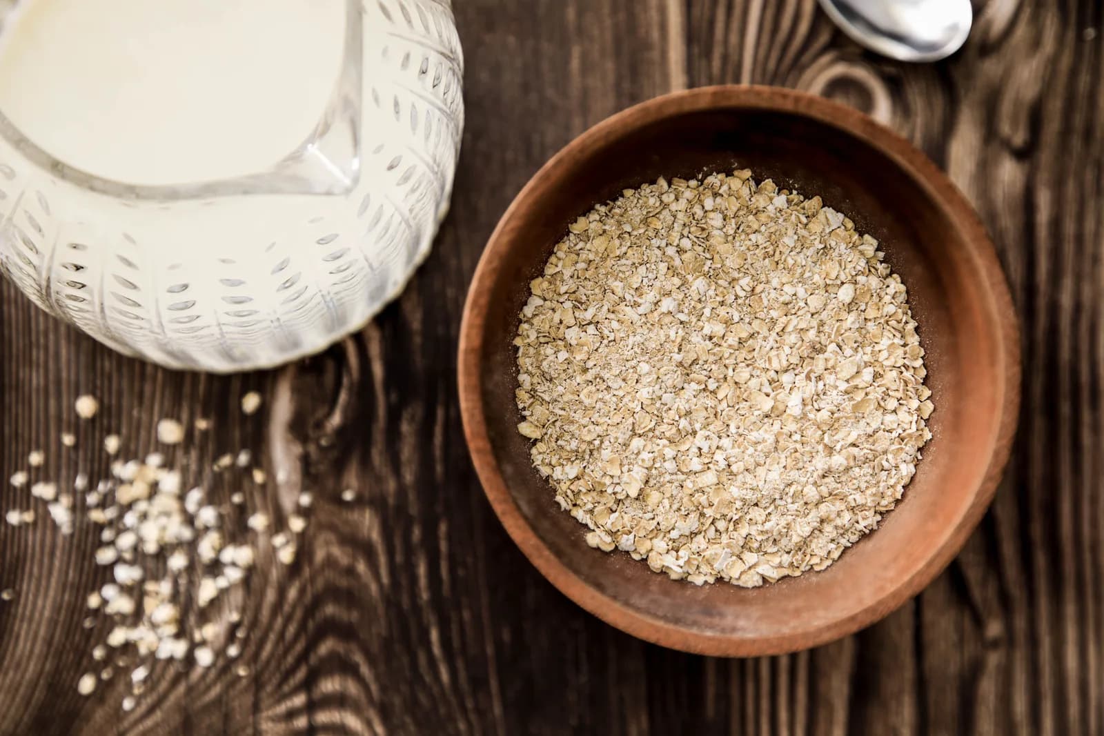 Rolled oats in a wooden bowl beside a jug of milk on a dark wooden table