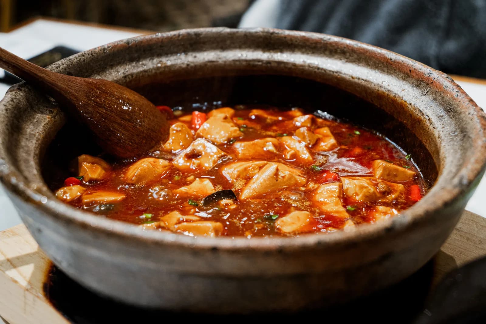 Tofu suave hirviendo en una salsa roja y aceitosa de chile en una olla de barro, con una cuchara de madera adentro