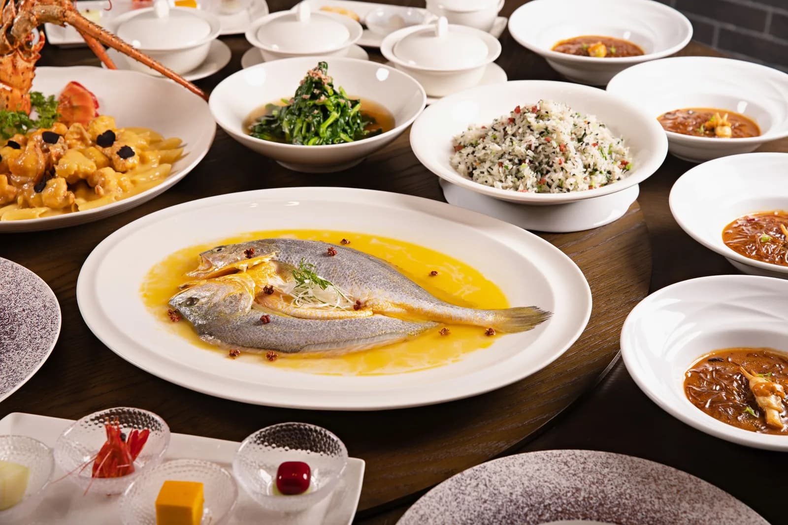 A Chinese banquet table with a whole fish in golden sauce at the centre, surrounded by small dishes and soups