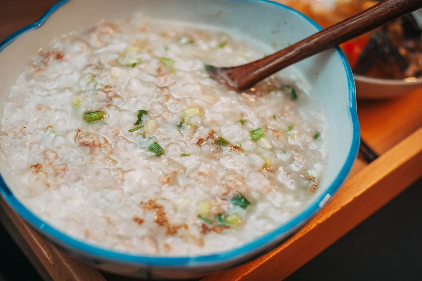 A bowl of rice congee with scallions and a wooden spoon