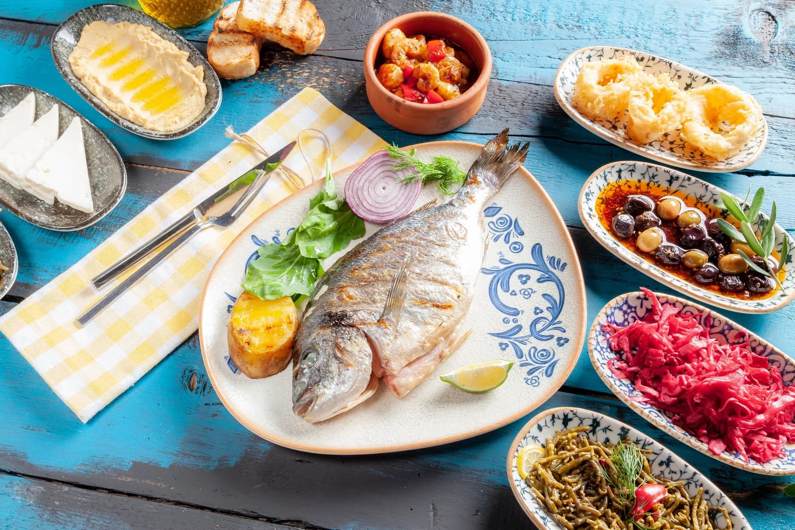 Grilled whole fish with small plates of meze on a blue wooden table