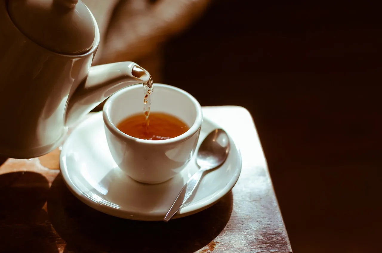Tea poured from a white pot into a cup on a dark wooden table