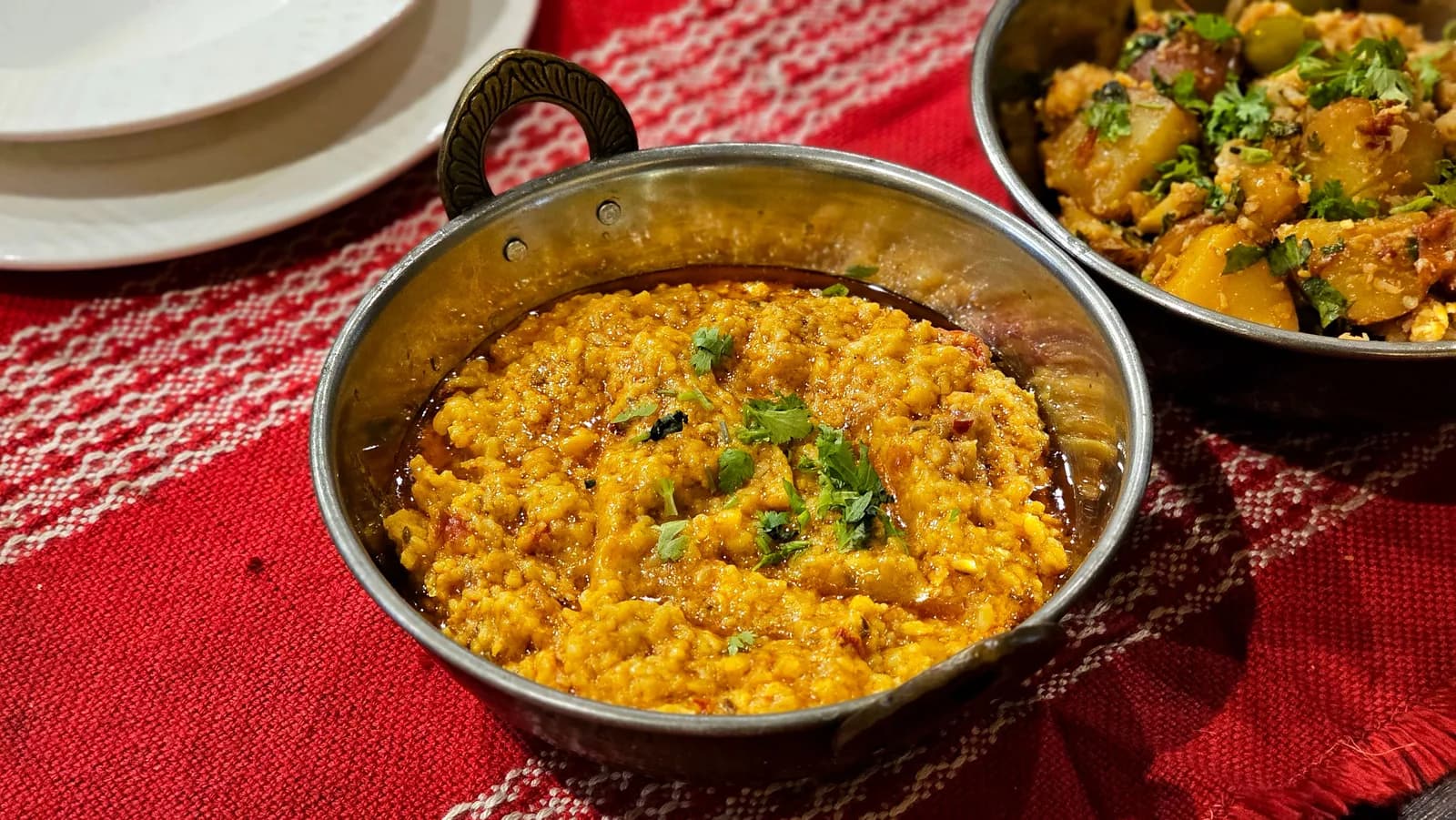 Dal amarillo con cilantro en un pequeño kadai de metal, junto a un guiso de verduras