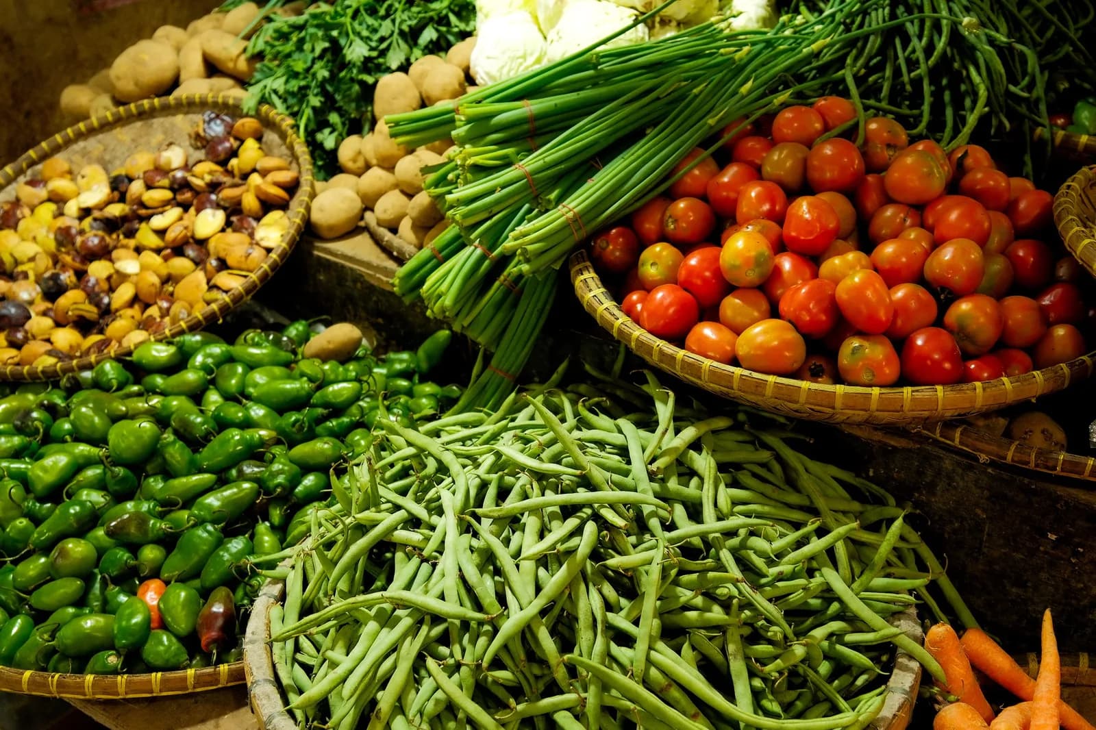Market baskets heaped with green beans, tomatoes, green chillies and spring onions
