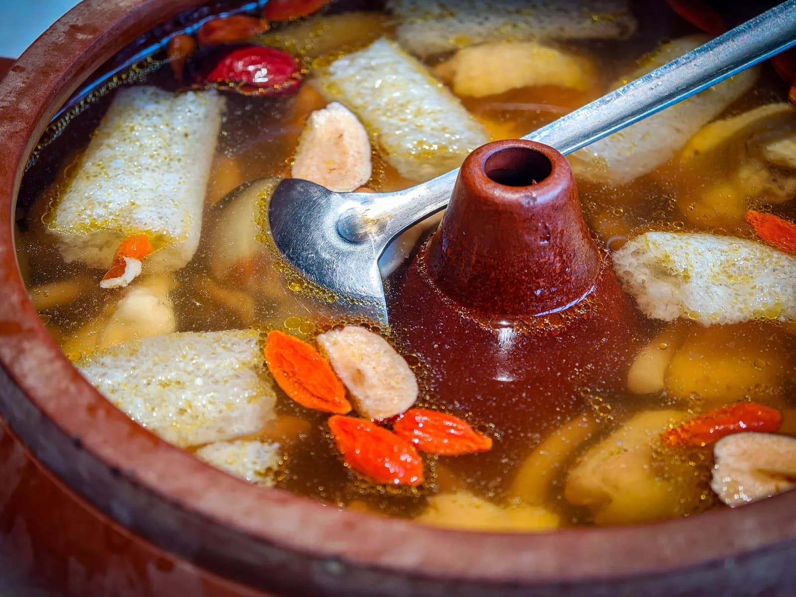 A clay pot of clear herbal broth with goji berries floating on top