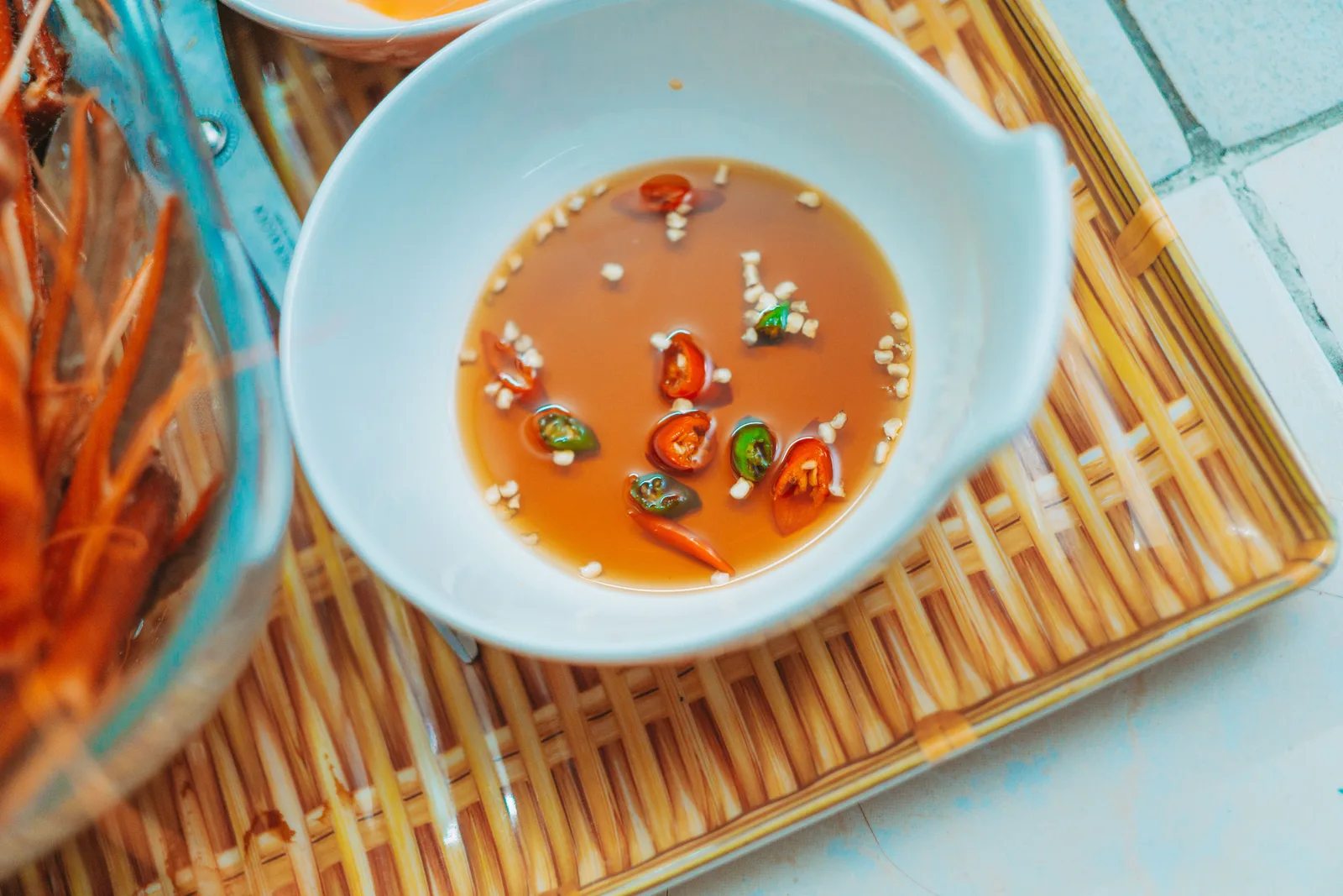 A bowl of fish sauce with sliced chillies and garlic on a bamboo tray
