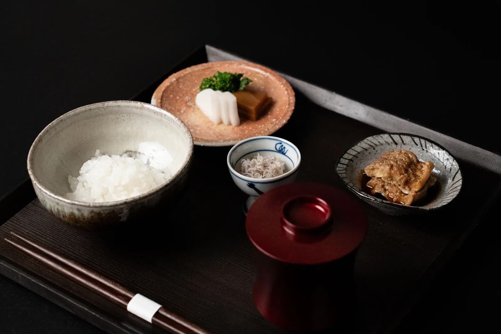 A Japanese breakfast tray with rice, a lidded lacquer soup bowl, a simmered dish, pickles and chopsticks