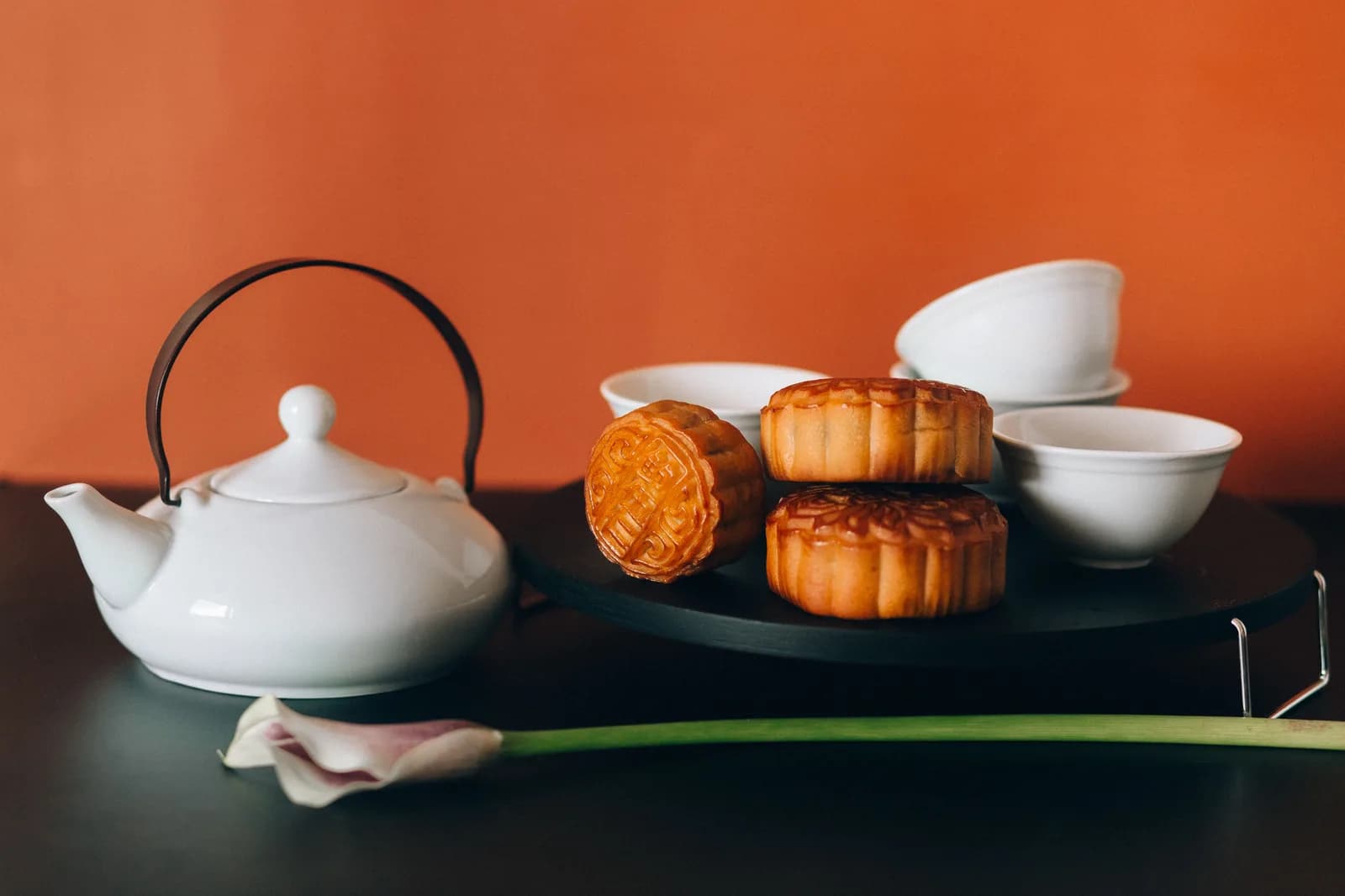 Mooncakes stacked beside a white teapot and teacups against an orange wall