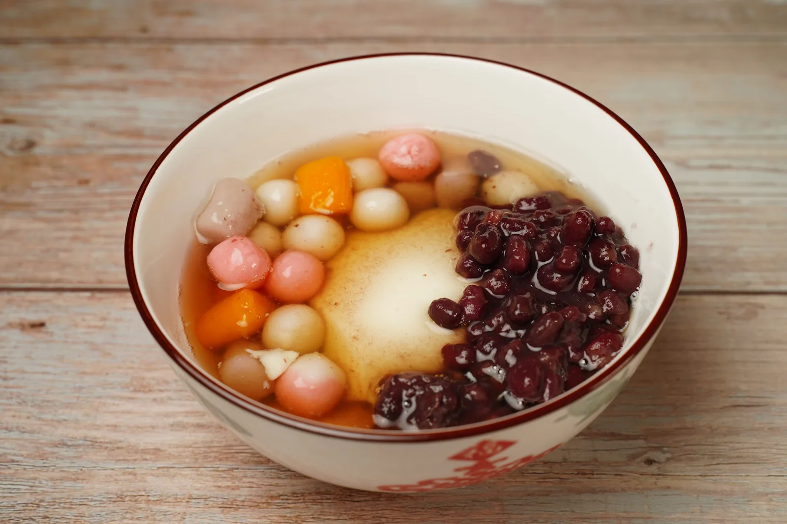 Red bean soup with small pink, white and orange glutinous rice balls in a white bowl