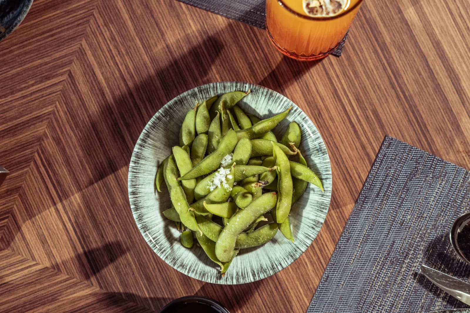 A bowl of salted edamame pods on a wooden table