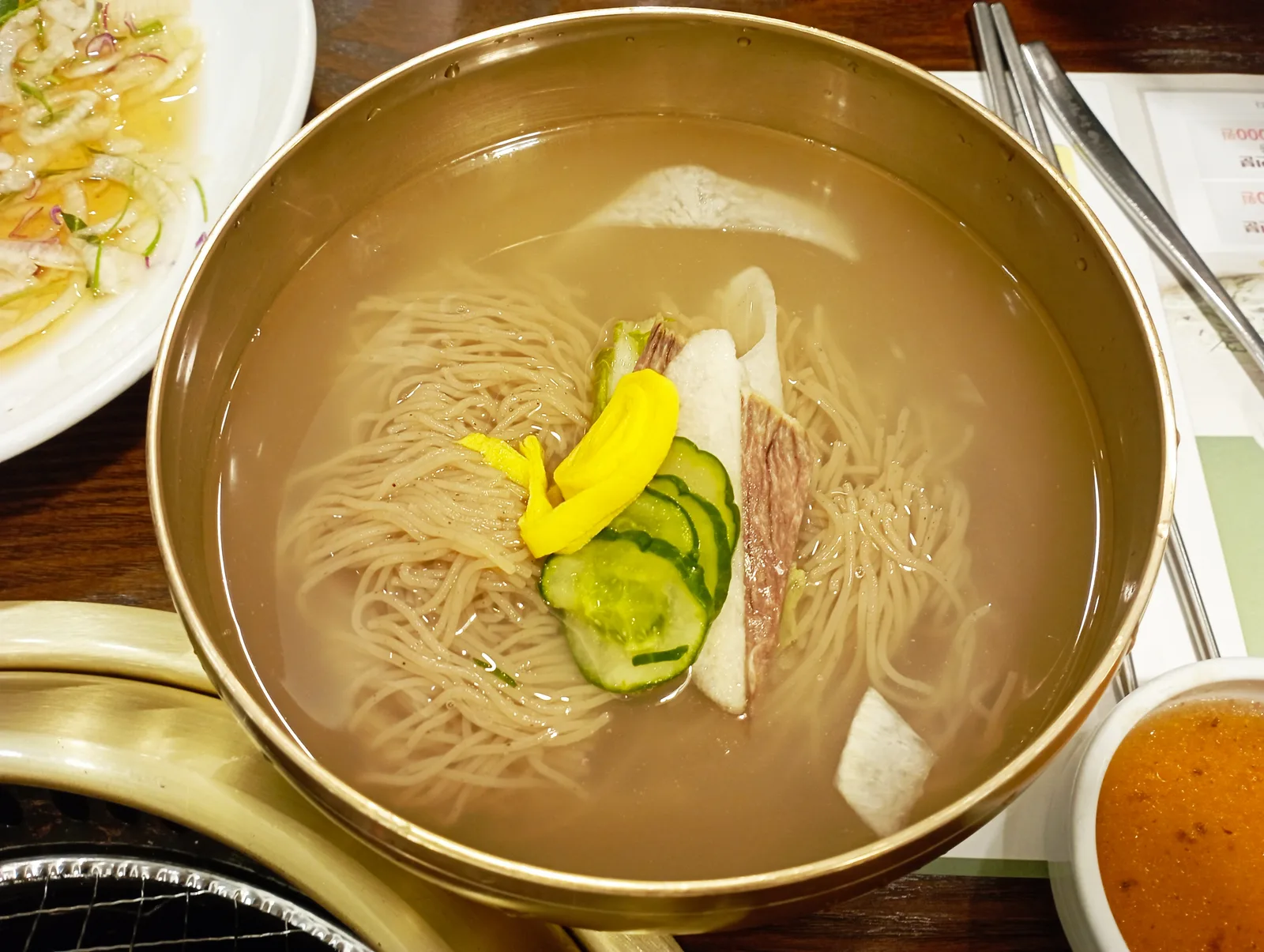 Mul naengmyeon in a brass bowl, buckwheat noodles in cold broth topped with cucumber, radish and a slice of beef