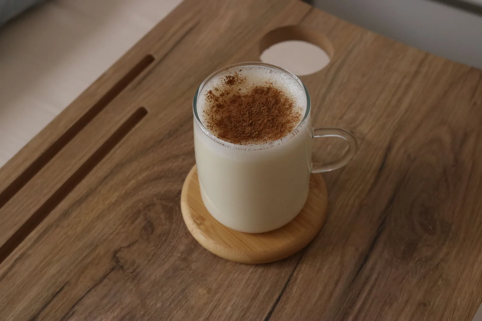 Un tarro de vidrio con leche tibia y espumosa espolvoreada con canela, sobre un posavasos redondo de madera