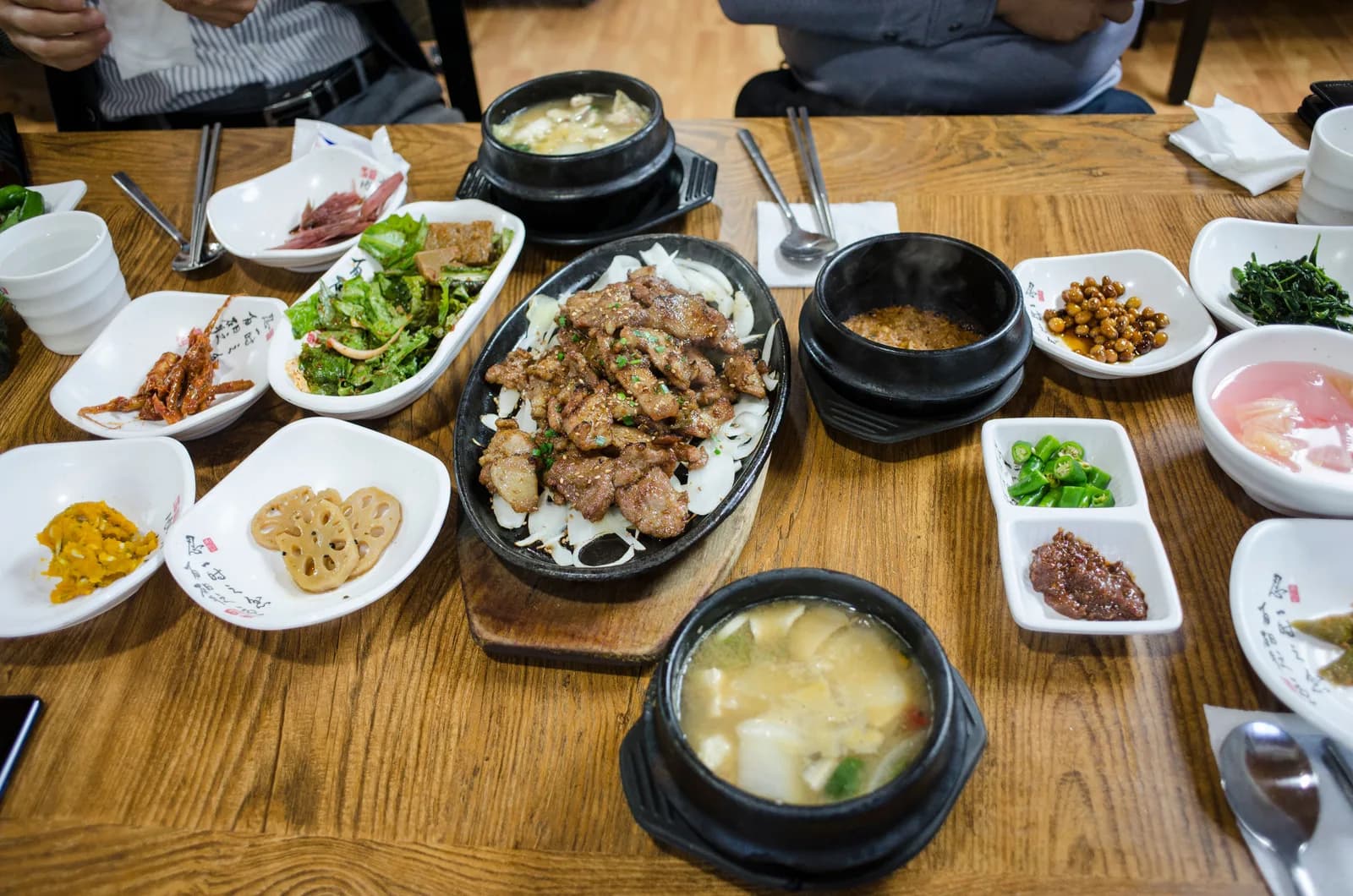 A Korean table laid all at once: grilled pork, bubbling stews in stone pots and a dozen small banchan dishes