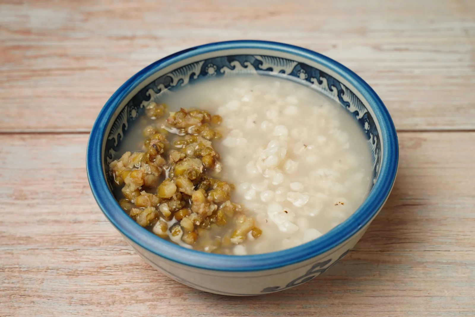 A blue and white bowl of soft rice porridge with a green topping heaped on one side
