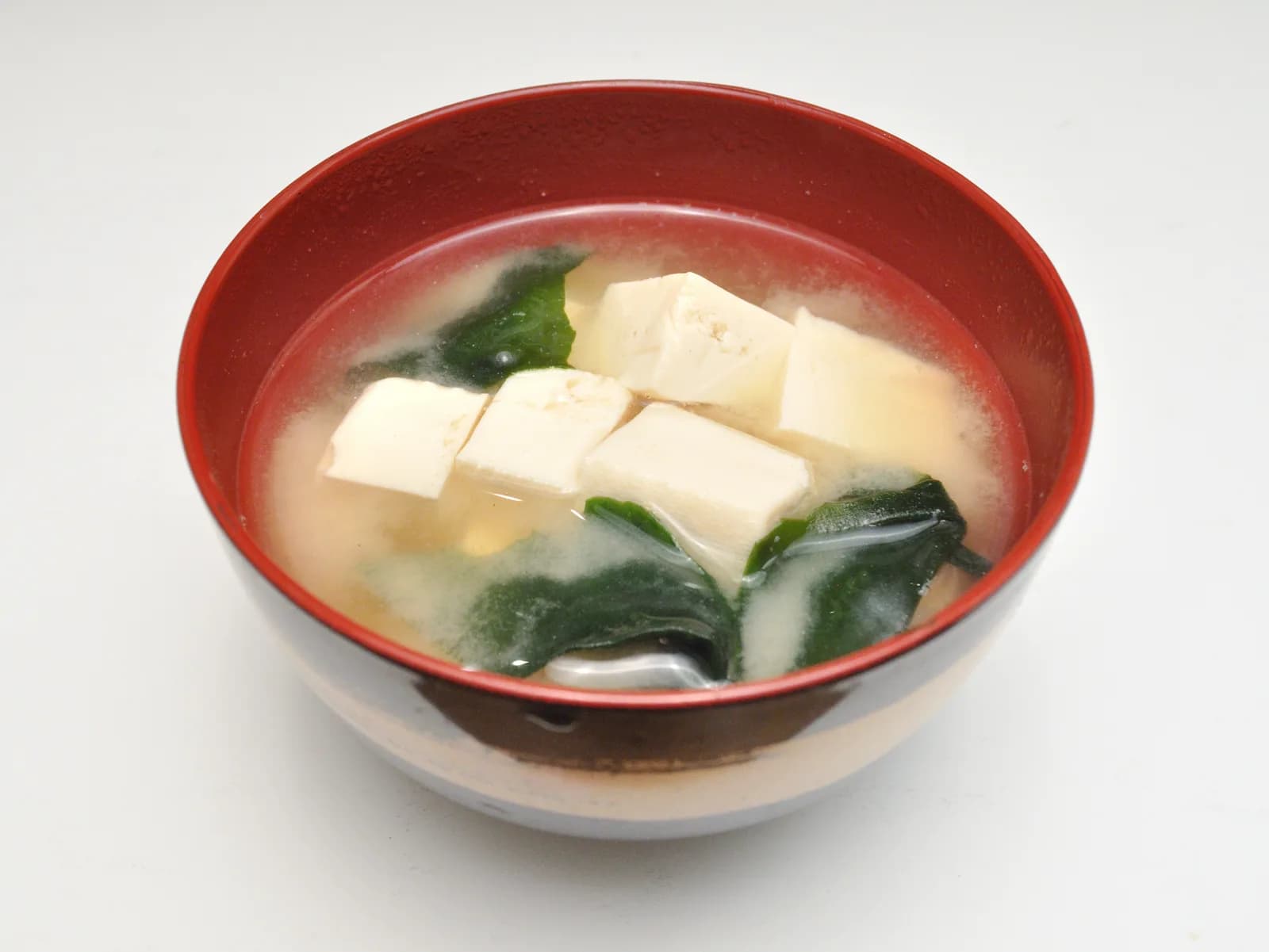 A red lacquer bowl of miso soup with cubes of tofu and wakame seaweed