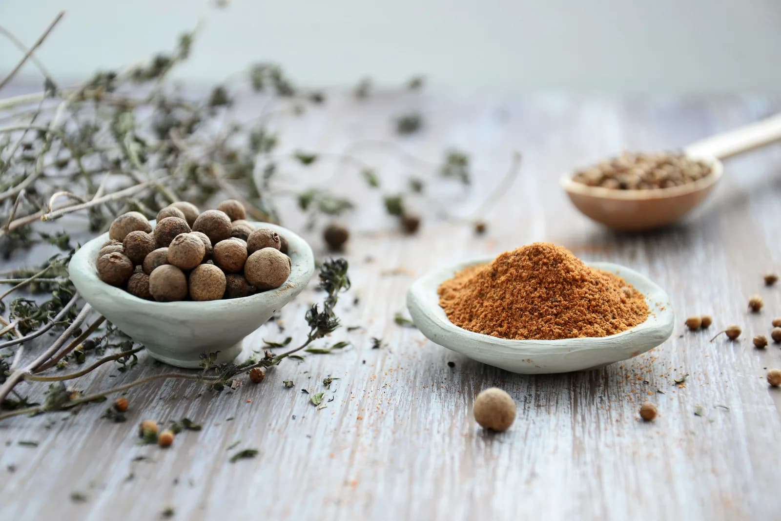 Whole allspice berries in one dish and a ground spice in another, with sprigs of dried herbs around them