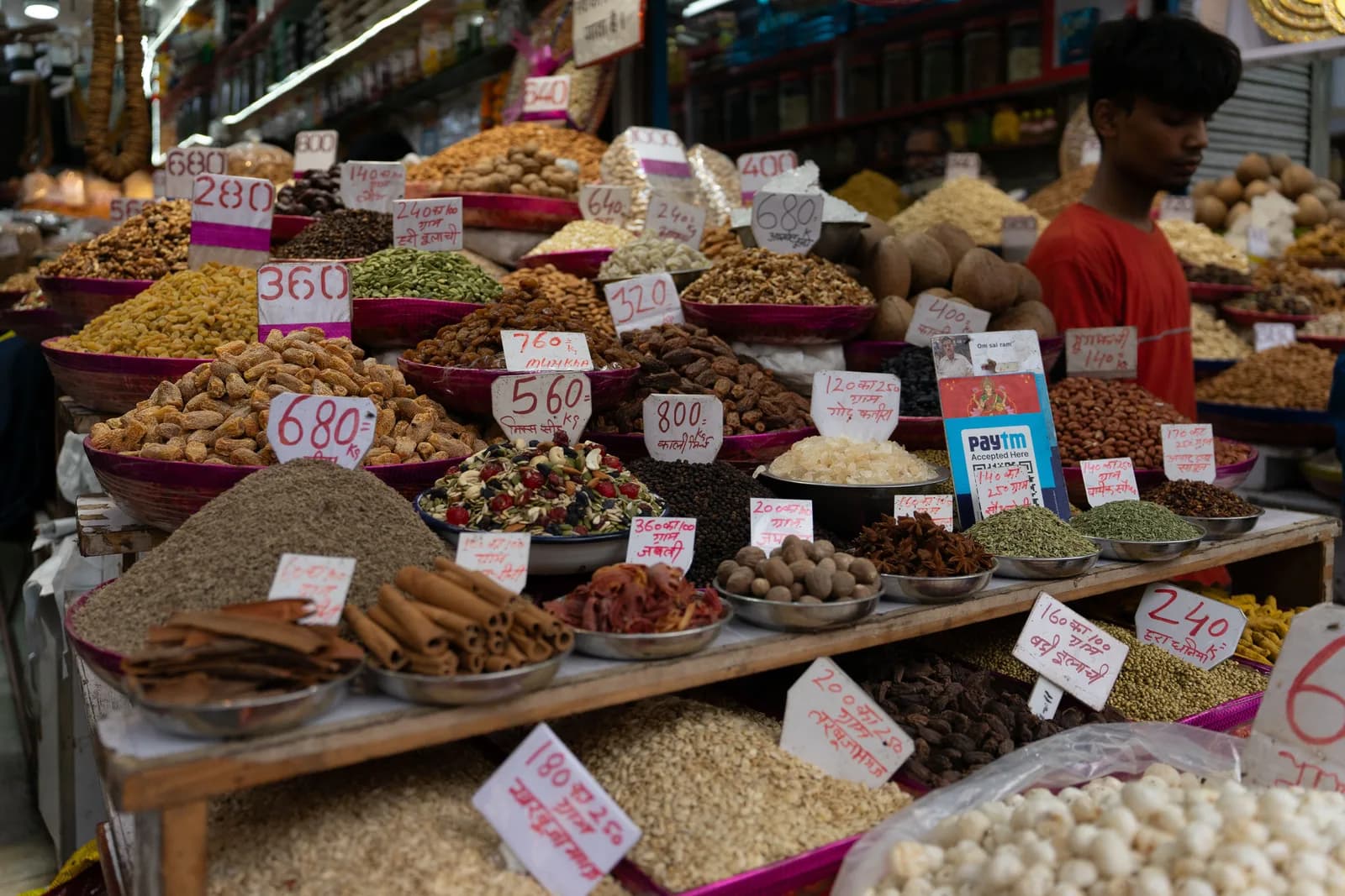 A spice stall in an Indian market, with heaps of whole spices, dried fruit and nuts under handwritten price tags